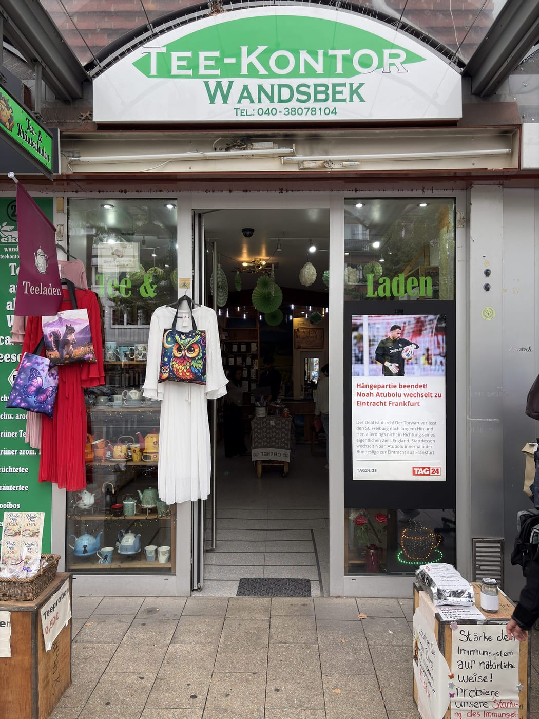 Ladenfront des Tee-Kontors Wandsbek mit grünem Schriftzug über dem Eingang und dekoriertem Schaufenster.