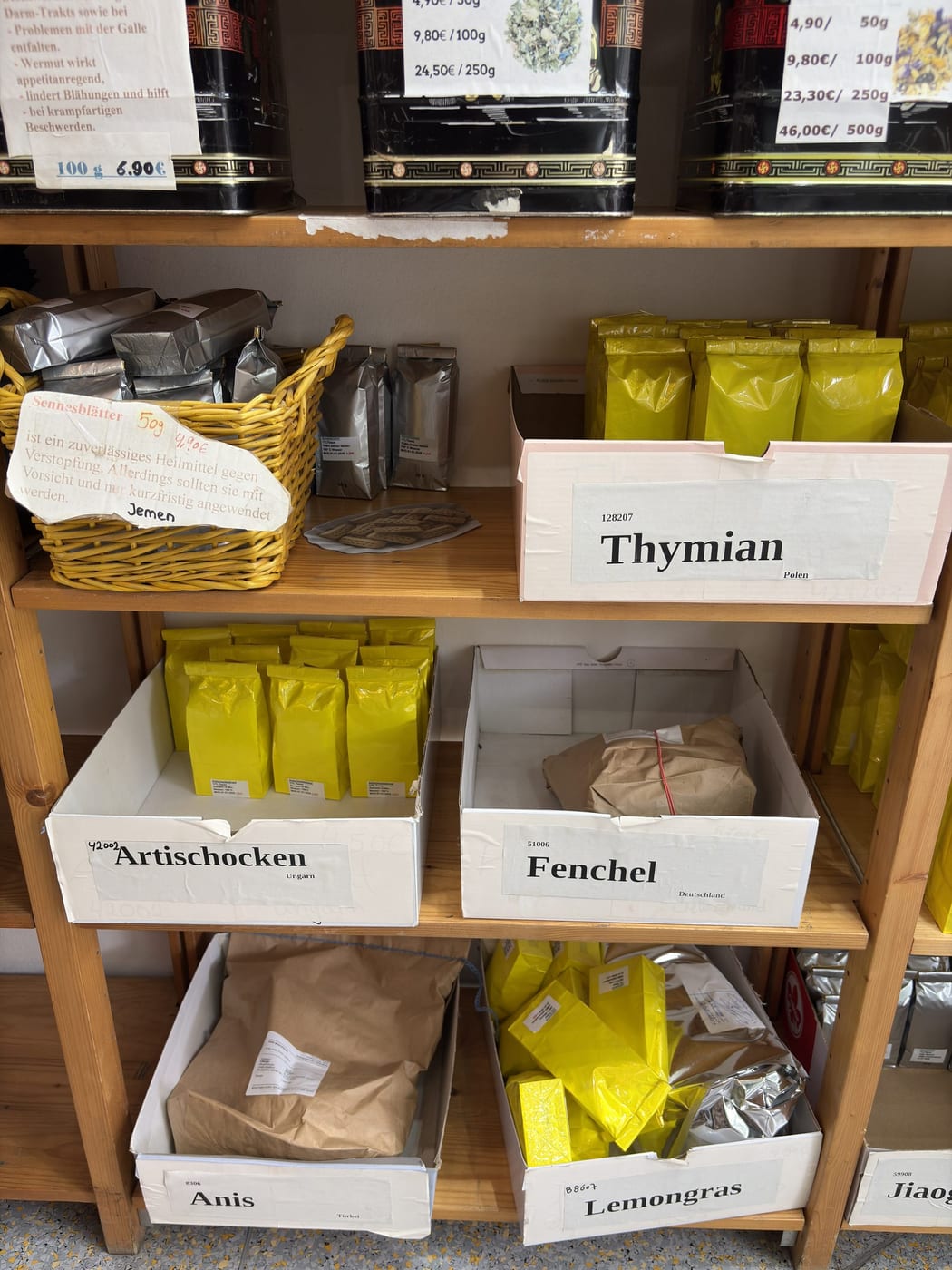 Kräuterregal mit beschrifteten Holzkisten: Thymian, Artischocken, Fenchel, Anis und Lemongras.